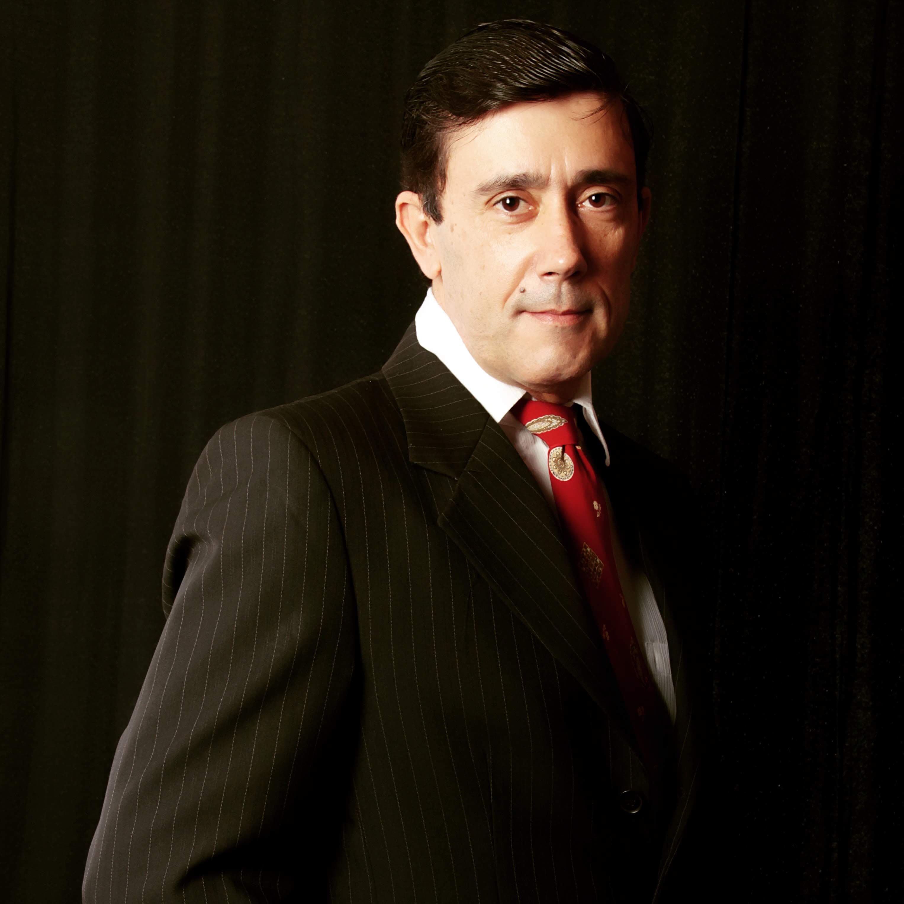 Retrato de Ricardo Machado Alencar vestindo terno escuro risca de giz com gravata vermelha